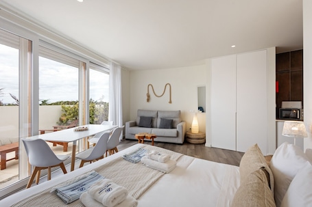 A modern hotel room with a large window, a sofa, a dining table with chairs, a bed with towels, a lamp, and a microwave.. Best Houses 89 - A Paixão da Moleira - Sotavento