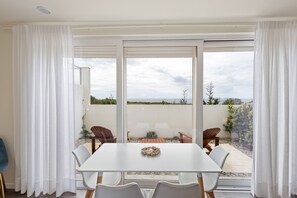 Zona pranzo con tavolo e sedie bianche, vista sull'esterno e una porta scorrevole in vetro.