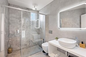 Ein modernes Badezimmer mit einer Duschkabine, einem weißen Waschbecken und einem großen Spiegel.