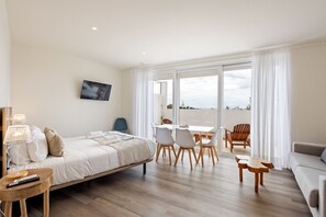 Ein modernes Hotelzimmer mit Bett, Nachttisch, Fernseher und einem Balkon mit Tisch und Stühlen.
