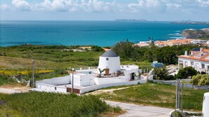 Un edificio costiero con facciata bianca e tetto a cono, immerso nel verde e con vista sul mare.