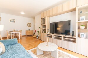 Ein modernes Wohnzimmer mit Fernseher, Holzschränken, einem Essbereich und einem blauen Sofa.