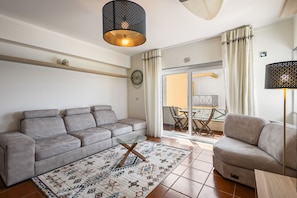 Ein Wohnzimmer mit grauem Sofa, einem gemusterten Teppich, einem Holztisch und einer Deckenleuchte.