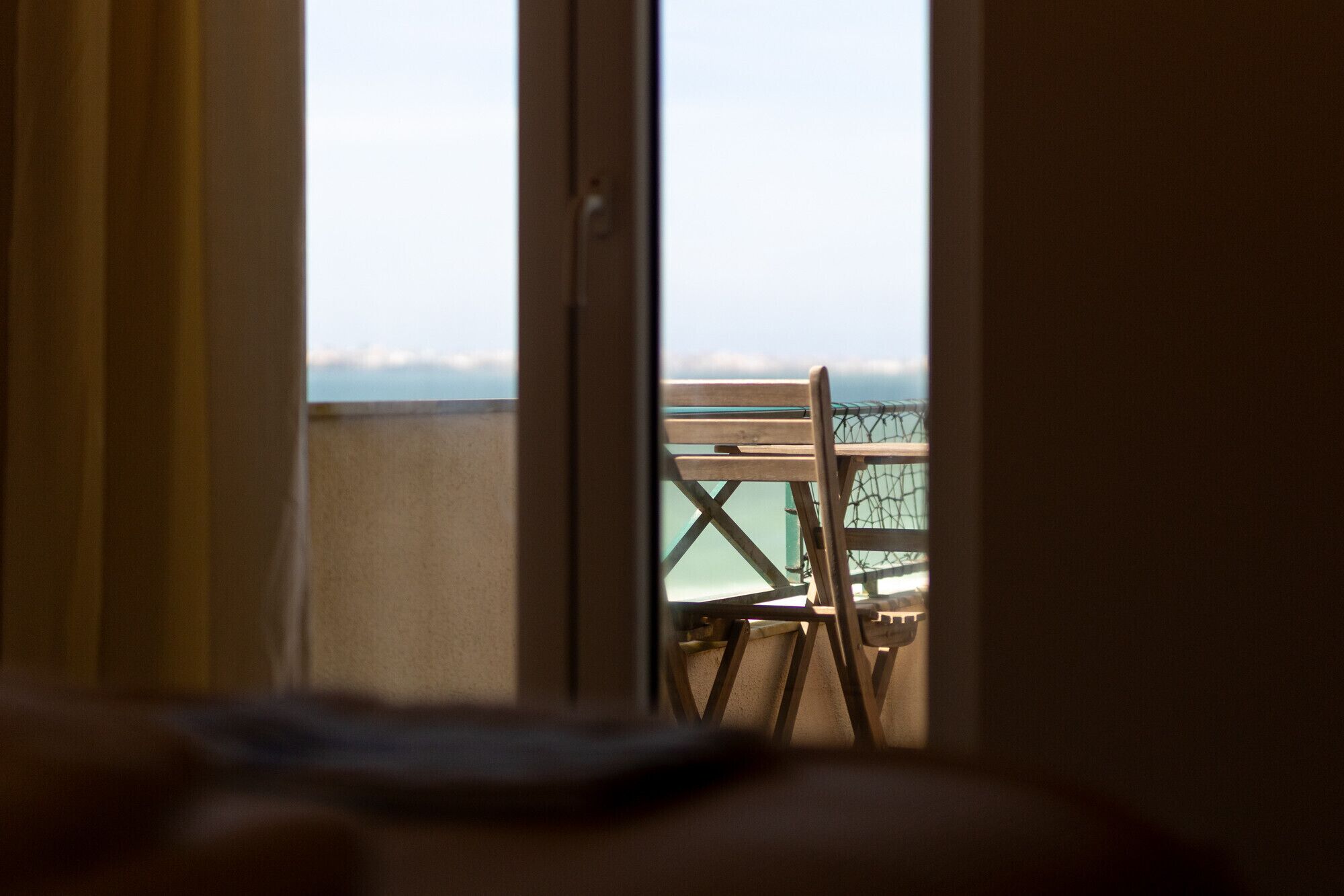 Quarto com vista para o mar através de uma janela, uma cadeira de madeira e uma mesa.
