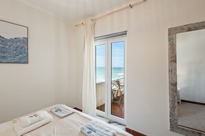 Ein Zimmer mit einem Bett, Blick auf das Meer durch eine Schiebetür, einem gerahmten Kunstwerk an der Wand und einem Holztürrahmen.