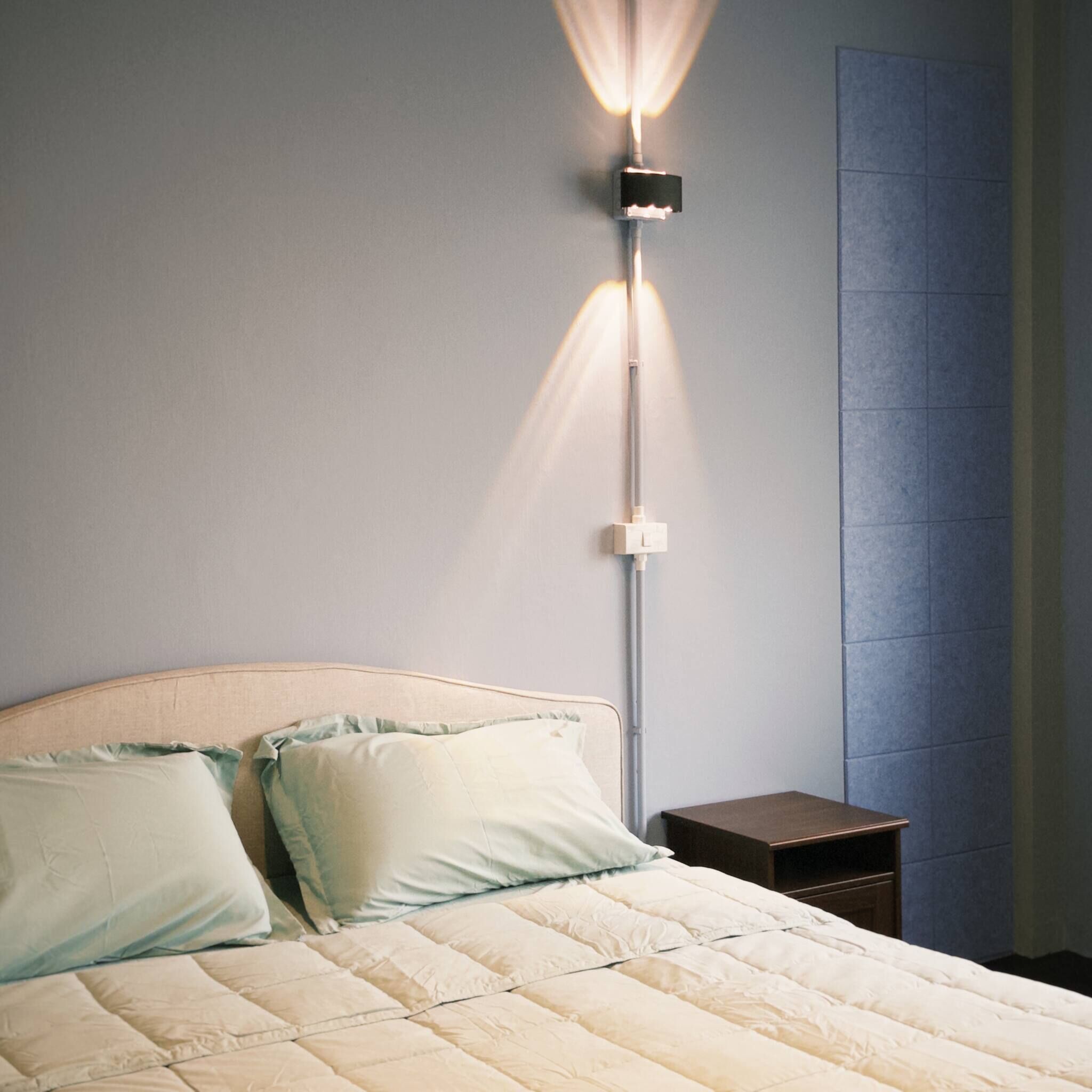 A bed with a headboard, pillows, a bedside table, and a wall-mounted light fixture.
