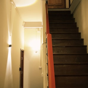 Una escalera con barandilla, una puerta y un aparato de luz.