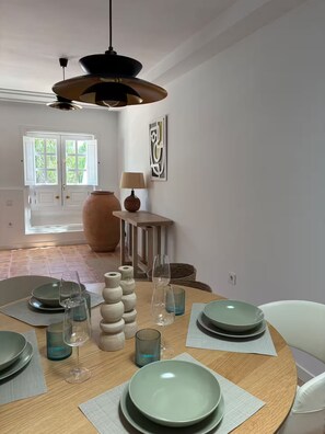 A dining area with a round table set for four, a hanging light fixture, a door with glass panels, and a wall-mounted abstract art piece. - Cesar's Oasis (Costa Teguise)