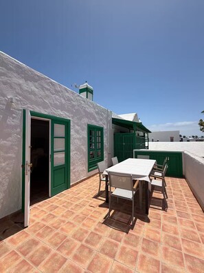 A patio with a table and chairs, a green door, and a white building with a chimney. - Cesar's Oasis (Costa Teguise)