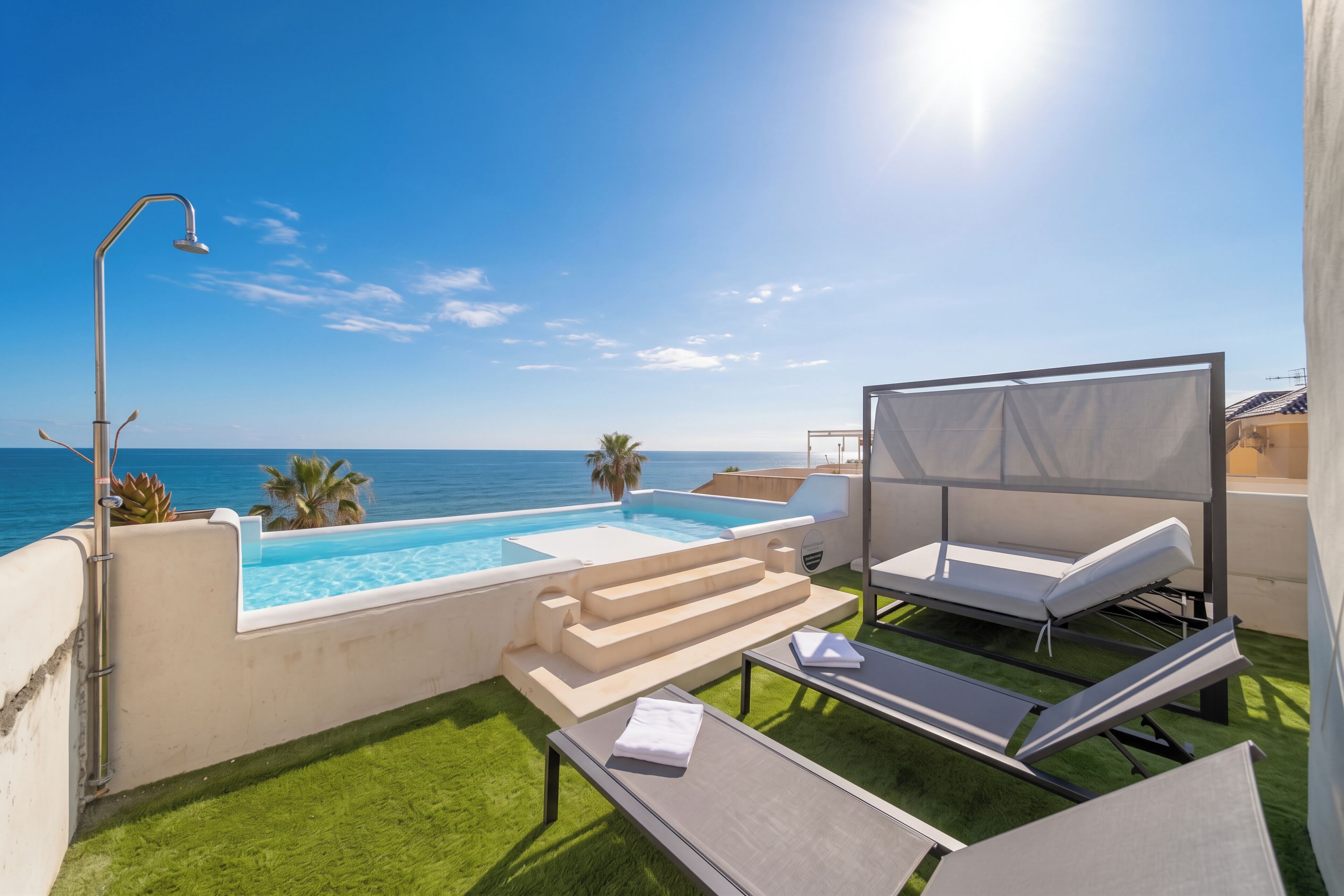 Un espace piscine aménagé sur le toit, offrant une vue dégagée sur l’océan, avec une douche et des chaises longues.
