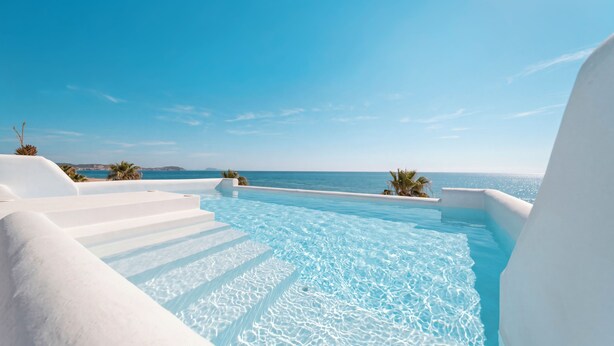Un cielo azul despejado, una piscina con escalones de acceso y vista al mar.