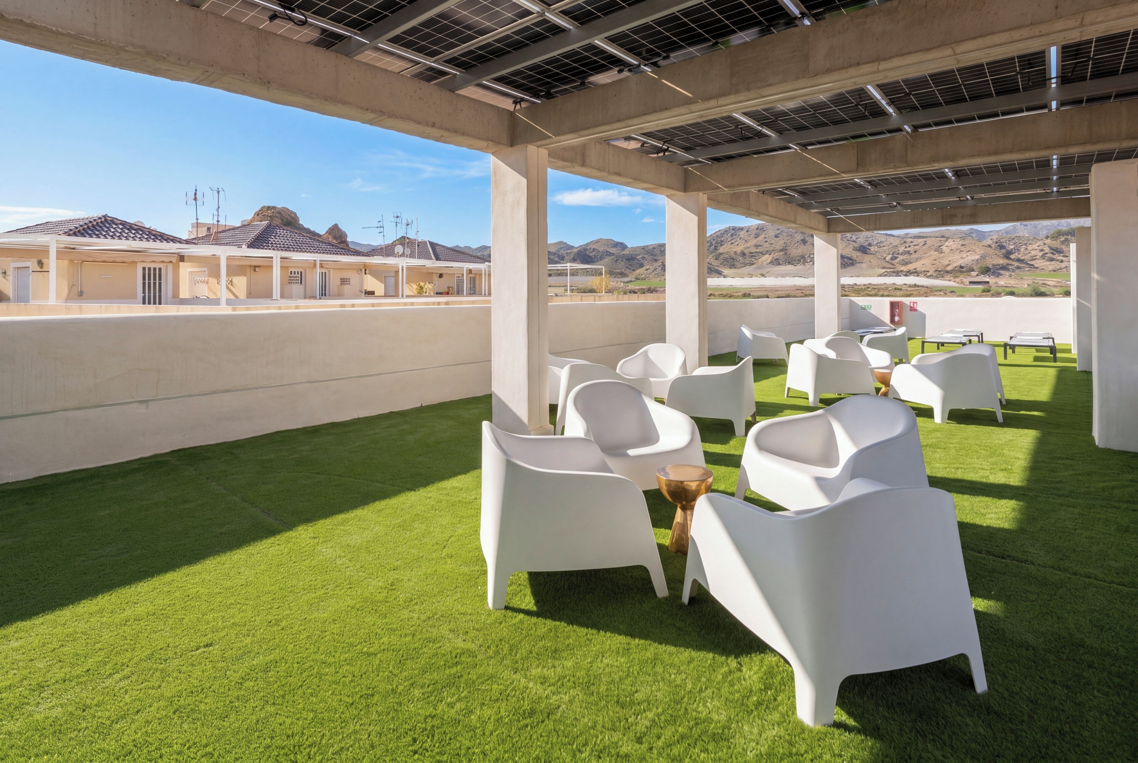 A rooftop terrace with artificial grass, white chairs, and tables.