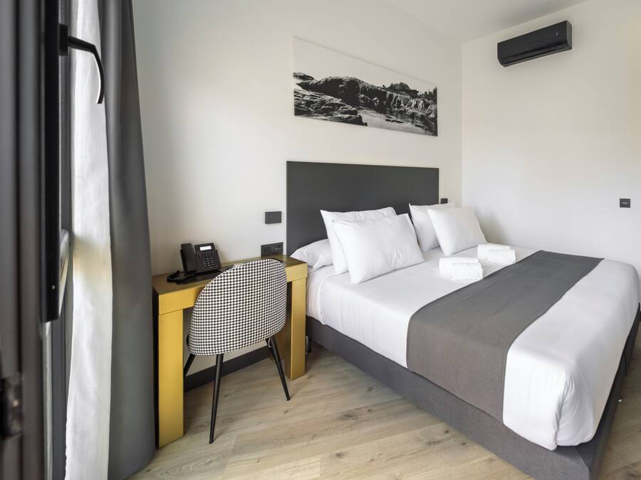 Una habitación de hotel con cama, escritorio con teléfono, silla, un cuadro en la pared y un armario.