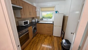 A compact kitchen with wooden cabinets, a microwave, a washing machine, and a refrigerator. - Erskine - House - Sleeps 4 - Parking - River Side (Erskine)
