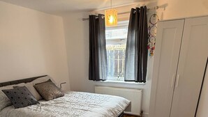 A bedroom with a bed, a window with curtains, a radiator, and a wardrobe. - Erskine - House - Sleeps 4 - Parking - River Side (Erskine)