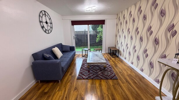 A living room with a sofa, a coffee table, a rug, a clock, and a patterned wall. - Erskine - House - Sleeps 4 - Parking - River Side (Erskine)