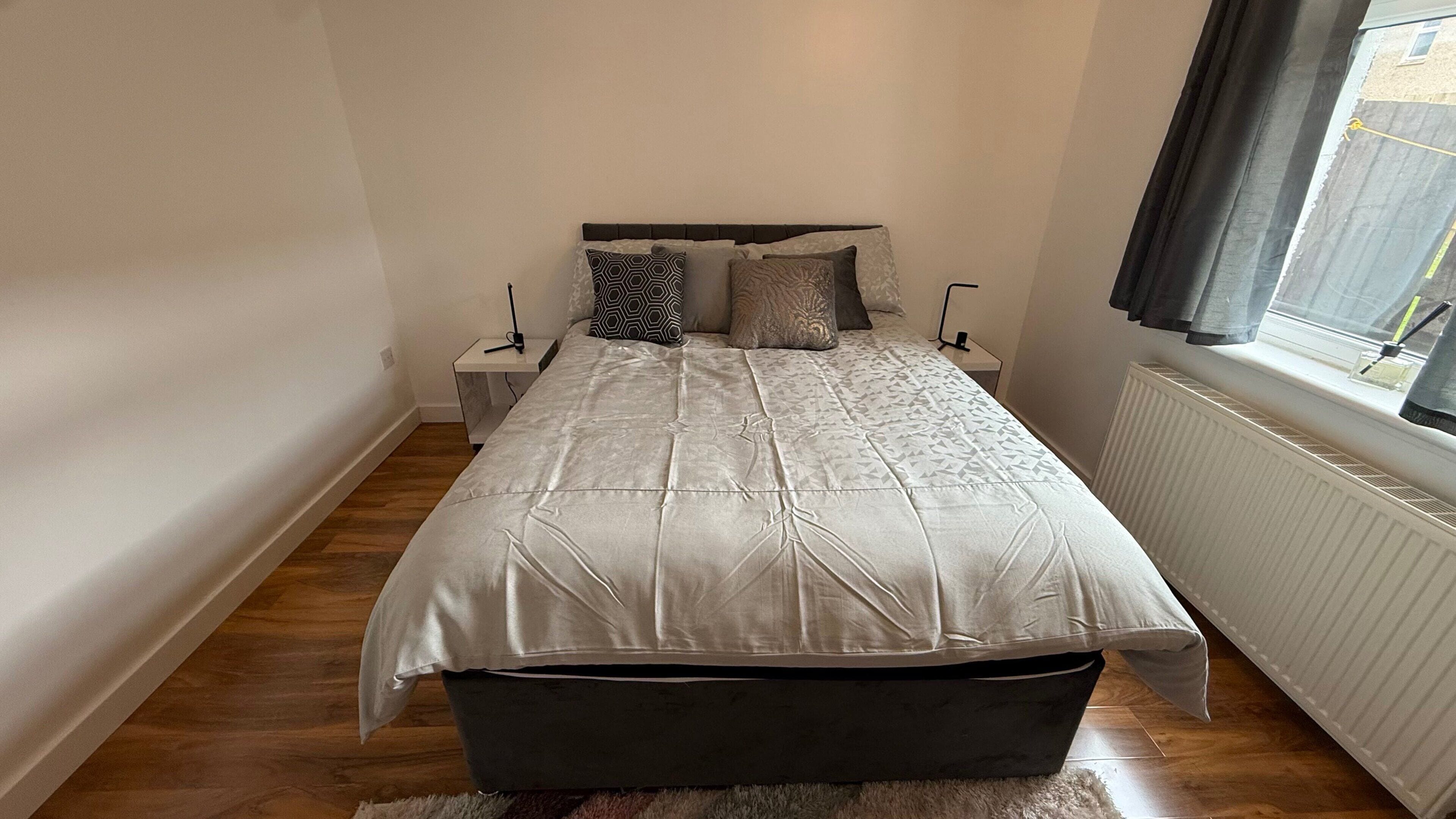 Ein Schlafzimmer mit Bett, Nachttischen, Heizkörper und einem Fenster mit Vorhängen.