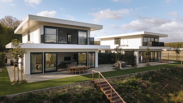 Una casa moderna de dos pisos con techo plano, grandes ventanales y una terraza de madera.