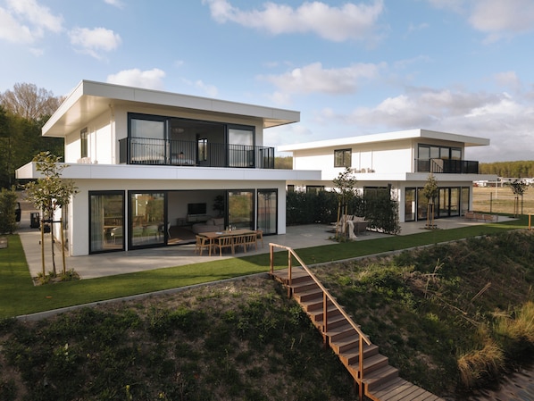 A modern two-story house with a flat roof, large glass windows, and a wooden deck.