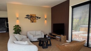 Una sala de estar moderna con sofá, sillón, mesa de centro, televisor y una planta.