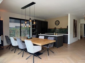 A modern kitchen with a central island, pendant lighting, and a dining area with a wooden table and chairs.