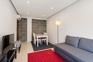 Ein modernes Wohnzimmer mit einem grauen Sofa, einem roten Teppich, einem Essbereich mit Tisch und Stühlen sowie einem Fernseher.