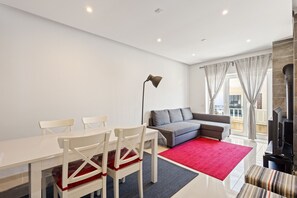 Ein modernes Wohnzimmer mit Esstisch, Stühlen, einer Couch, einem roten Teppich und einem Kamin.