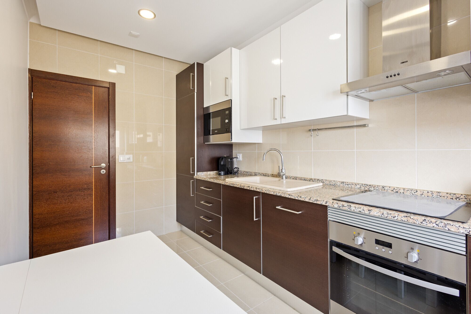 Een moderne keuken met een houten deur, roestvrijstalen apparatuur en een wit aanrecht.