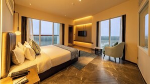 Een moderne hotelkamer met een groot bed, een televisie, een zithoek en uitzicht op zee.