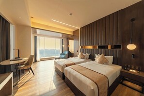 Une chambre d’hôtel avec deux lits, un bureau, une chaise et une grande fenêtre donnant sur un beau paysage.