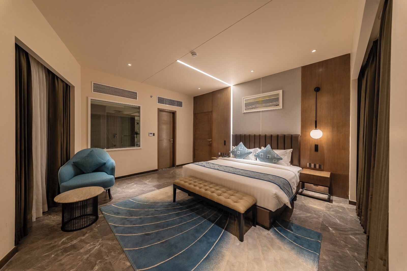 Une chambre à coucher moderne avec un lit, une chaise, un banc, un tapis et un tableau accroché au mur.