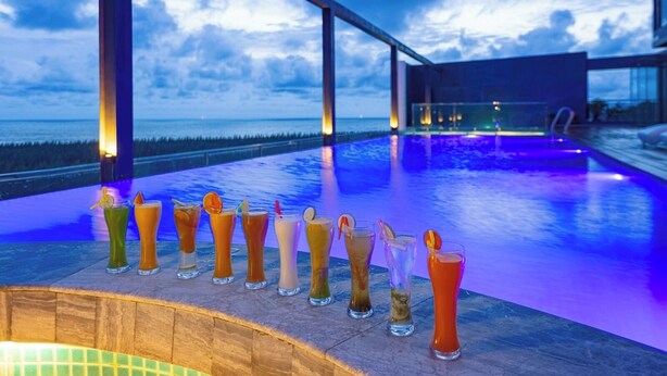 Een overloopzwembad met uitzicht op de oceaan, een bar met diverse drankjes en een modern architectonisch ontwerp.