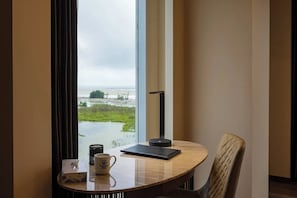 Una habitación con vista a un cuerpo de agua, una mesa con una taza, un libro y una lámpara.