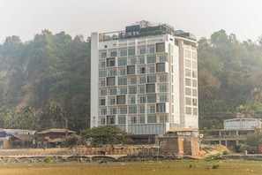 A multi-story hotel with a modern design, featuring a balcony on the upper floor and a view of a hilly landscape. - Bay Hills Hotel Ltd (Cox's Bazar)
