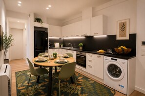 Eine moderne Küche mit weißen Schränken, einer schwarzen Arbeitsplatte, einer eingebauten Waschmaschine und einem Essbereich mit Tisch und Stühlen.