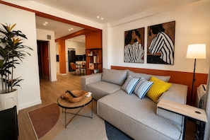 Ein modernes Wohnzimmer mit einer Couch, einem Couchtisch und einer Lampe. Ein Bücherregal und ein Topf mit einer Pflanze sind ebenfalls vorhanden.