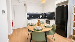 Une cuisine moderne avec des meubles blancs, un réfrigérateur noir et une table à manger pour quatre personnes.
