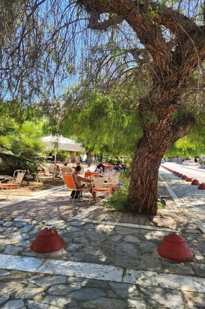 An outdoor seating area with stone flooring and red bollards, surrounded by trees and umbrellas. - LIV - Upscale Athenian Apartment 1B (Athens)