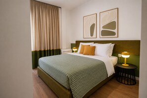 Habitación de hotel con cama, dos mesitas de noche, ventana con cortinas y arte abstracto en la pared.