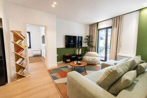 Una sala de estar moderna con un sofá, una mesa de centro, una estantería, un televisor y un ventanal con cortinas.