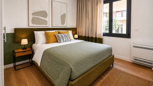 Une chambre bien rangée, avec un lit, des tables de chevet, une fenêtre avec des rideaux et des œuvres d’art accrochées au mur.