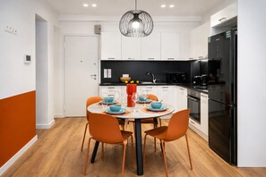 A modern kitchen with white cabinets, a black refrigerator, and a dining table with orange chairs. - LIV - Upscale Athenian Apartment 3B (Athens)