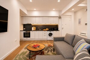 Eine moderne Küche mit eingebauten Geräten, ein Essbereich mit Tisch und Stühlen sowie ein Wohnzimmer mit einer Couch und einem an der Wand befestigten Fernseher.