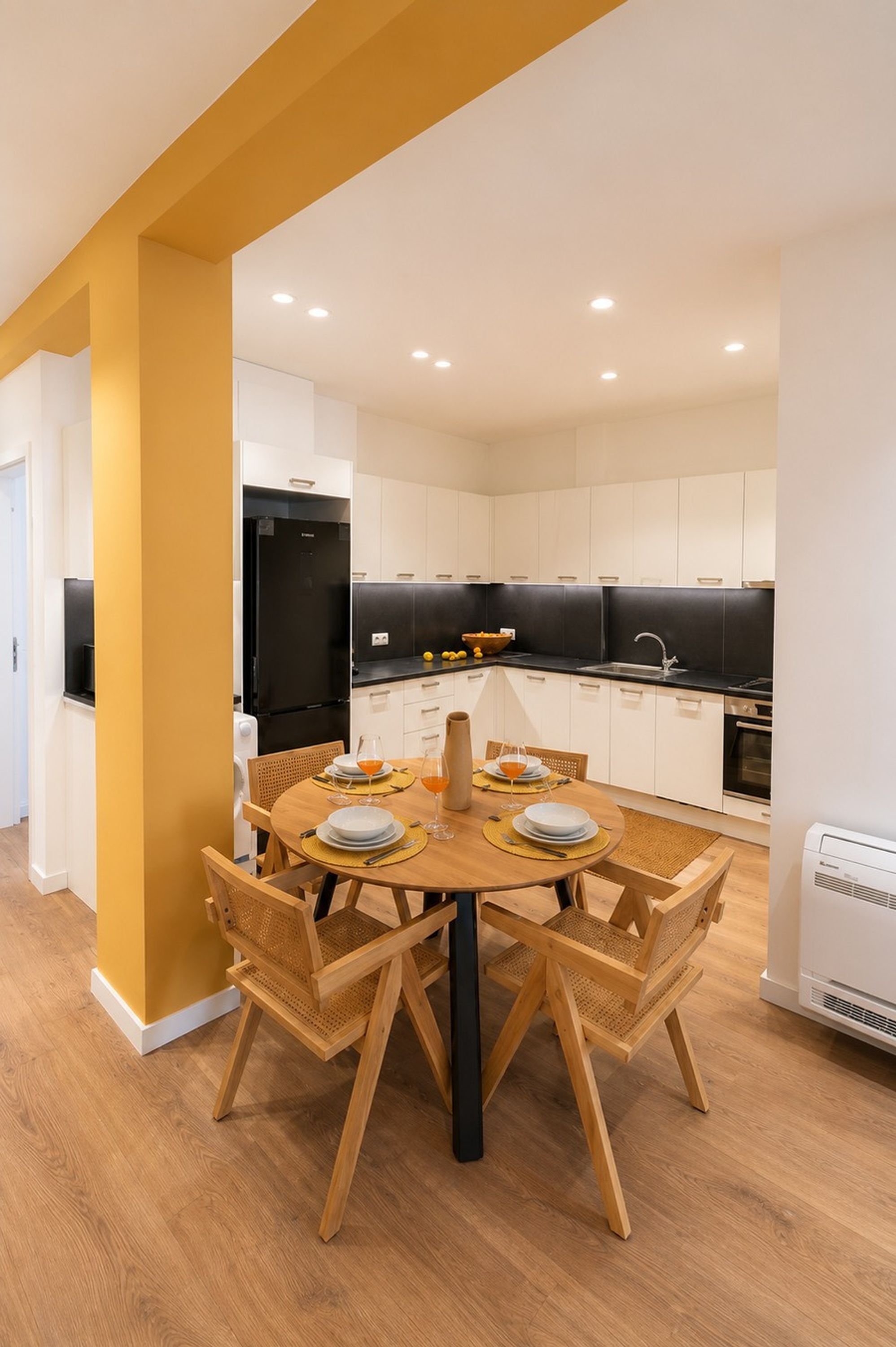 Une cuisine moderne avec des meubles blancs, un réfrigérateur noir et un coin repas comprenant une table et des chaises en bois.