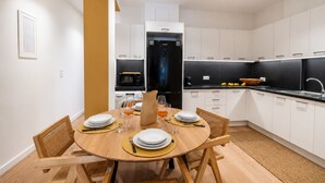 Una cucina moderna con mobili bianchi, un piano di lavoro nero e un'area pranzo con un tavolo rotondo per quattro persone.