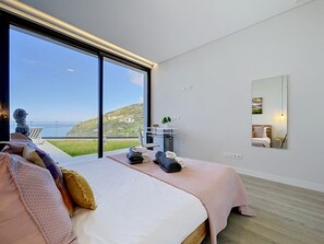 A bedroom with a large window, a bed with pillows, a bedside table with a plant, and a mirror on the wall. - Pearl of Madeira by Atlantic Holiday (Calheta)