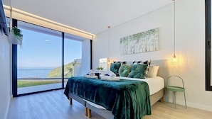 A modern bedroom with a large bed, a view of the outdoors, and a minimalist design. - Pearl of Madeira by Atlantic Holiday (Calheta)