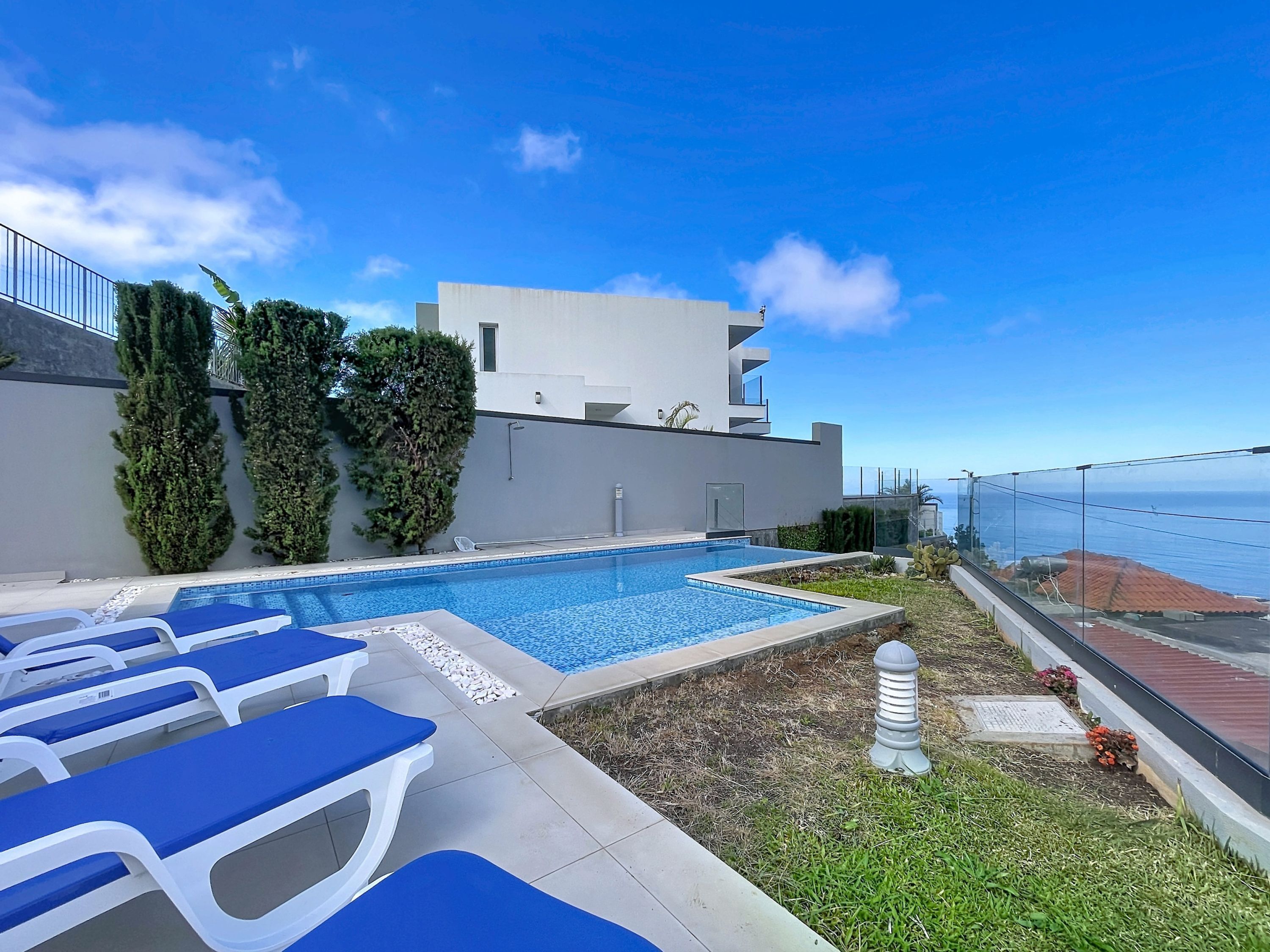 A modern pool area with lounge chairs, a clear view of the sea, and a building with a flat roof.