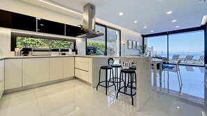 A modern kitchen with a central island, bar stools, and a view of the sea. - Pearl of Madeira by Atlantic Holiday (Calheta)