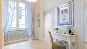 A room with a white desk, a chair, a framed picture, and a window with curtains. - The Gilded Residence (Lucca)